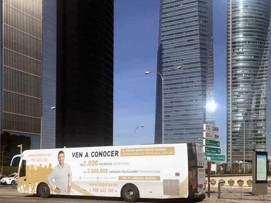 Bus blanco en la carretera con publicidad de autobuses para un evento.